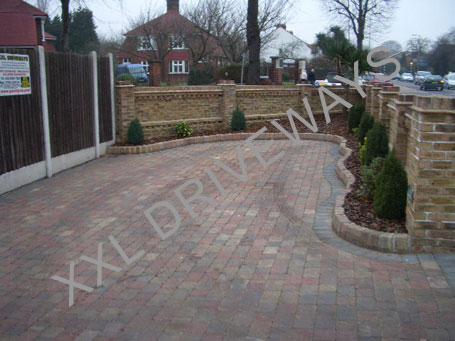 Process of a block paved driveway with flower bed, brick wall surrounding property.